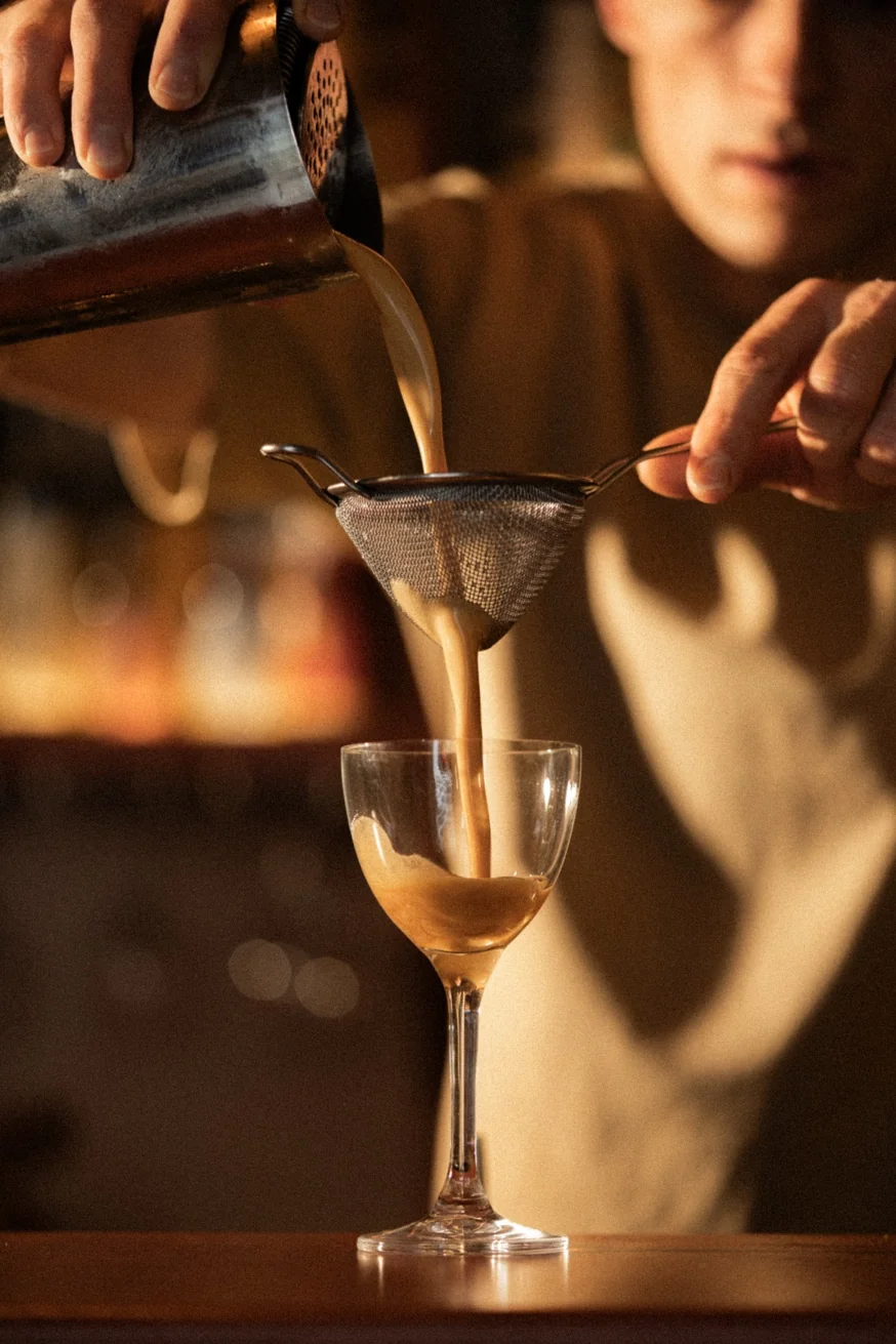 Bartender pouring a Mexpresso mezcal espresso martini through a fine mesh strainer at Pūblico Mezcaleria Mykonos